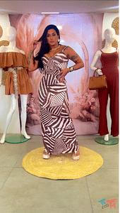 Mulher com vestido longo estampado em marrom e bege, com fundo boho chique.