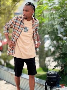 Modelo masculino usando camisa xadrez aberta, camiseta bege estampada e bermuda preta