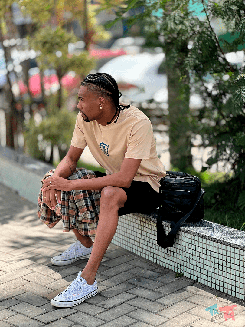 Look masculino com camiseta bege, short preto e tênis branco.